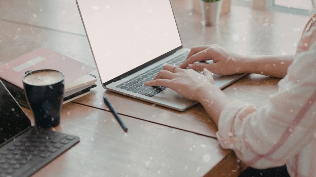 תקריב של ידיים עובדות על מחשב נייד על שולחן עץ מסודר, לצד כוס קפה ומחברות – ייצוג של ניהול אופרציה דיגיטלית ובק-אופיס.